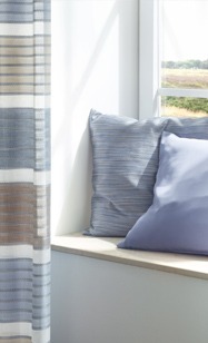 Dekostoff Kissen blau und grau am Fenster mit Vorhang blau und braun