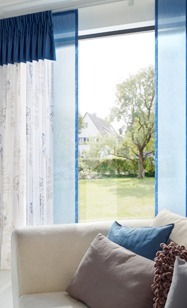 Sofa besch mit blau und grauen Kissen, Ansicht auf Fenster mit blauen Flaechenvorhang